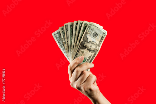 Hand holding US dollar bills on red background. Man holding cash money, concept of finance, payment, cost of living, emergency fund, or winning.