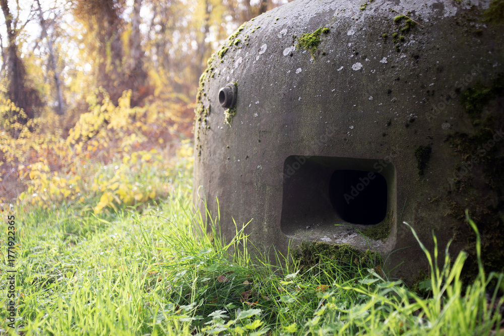 Fototapeta premium Wielka gruba stalowa kopuła starego powojennego bunkra stanowiąca pancerz ochraniający żołnierza na tle jesiennych barw