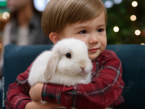 Little boy hugging white rabbit indoors with festive lights