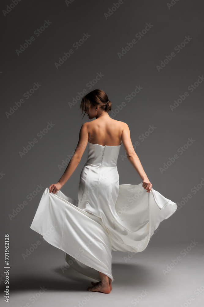 Naklejka premium Elegant bride in minimalist white dress twirls in modern studio with soft natural light