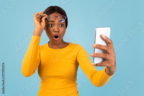Photography A woman wearing a yellow long-sleeve shirt is holding her smartphone, displaying surprise