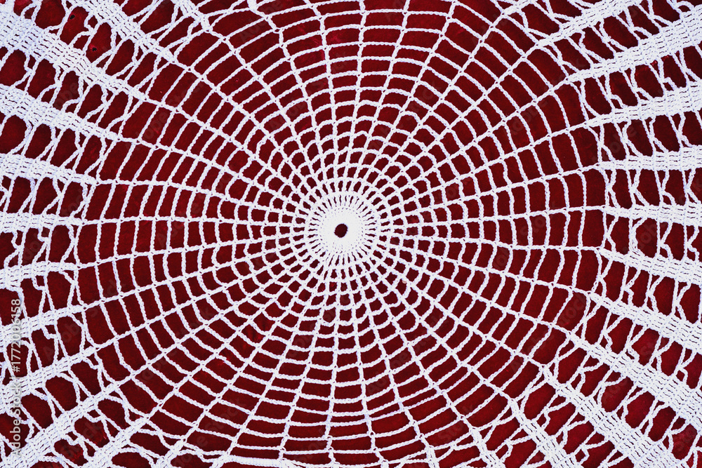 Fototapeta premium White crochet doily in circular geometric pattern placed on red background. Concept of handmade art, vintage style, traditional style. Craft background