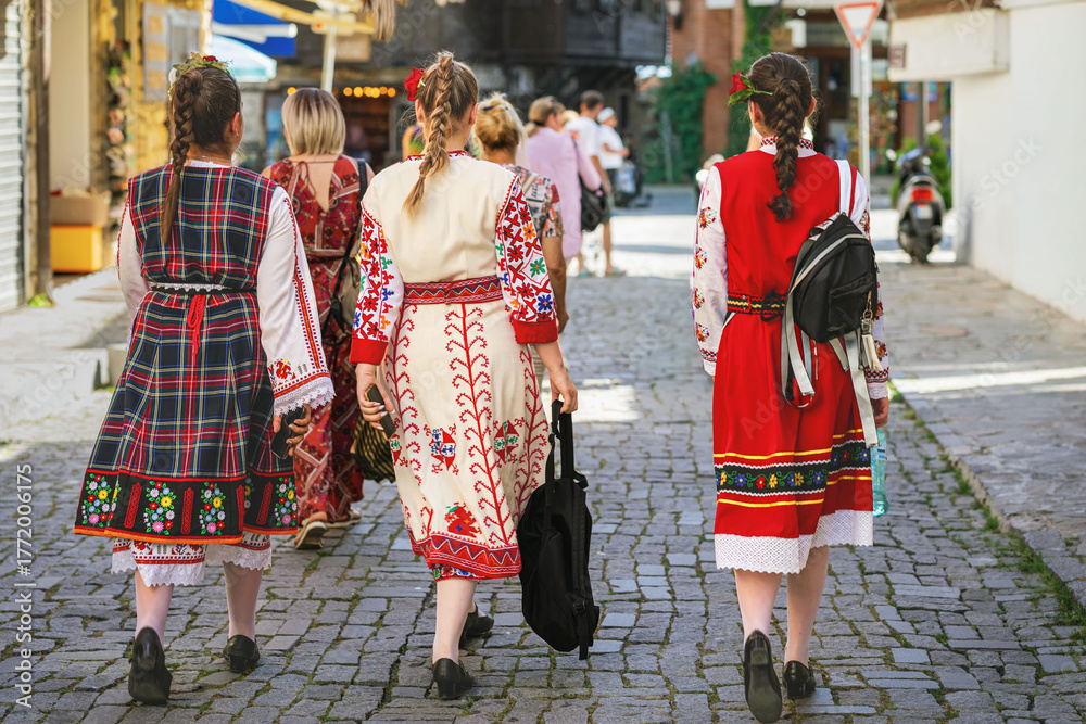 Fototapeta premium Women wearing traditional Bulgarian folk costumes walking on cobbled street during cultural event. Concept of heritage, folklore and national identity