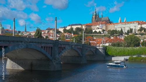 View of Prague from the river. Modern boat sailing along vltava river near manes bridge, with prague castle rising majestically under clear blue sky, capturing iconic heritage landscape