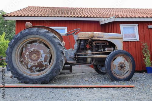 Old traditional tractor vehicle. Red house in the background.