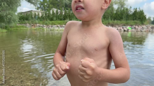 Child standing wet on lake shore shaking from cold after swimming summer outdoor nature water fun emotion health