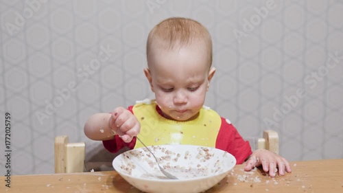 A super cute little toddler is joyfully eating from a colorful bowl, creating a delightful meal time mess