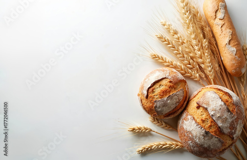 Fresh baked artisan bread loaves, golden wheat stalks rest on clean white background. Rustic bakery products promote natural organic food concept. Healthy whole grain flour ingredients from farm