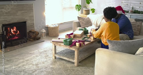 Gathering supplies, African American couple wrapping presents on coffee table for holiday season