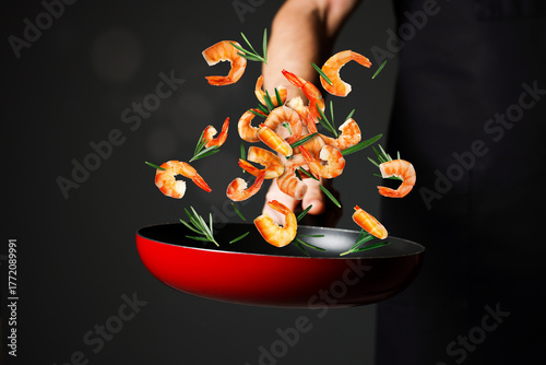 Quadro su tela Chef tossing shrimps and rosemary in pan against black background, closeup