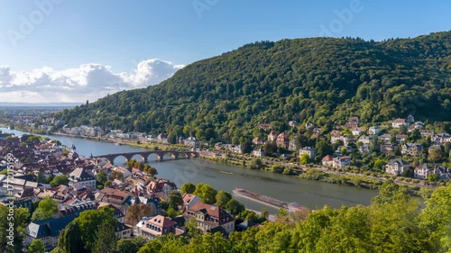 Timelapse of Heidelberg cityscape with river and bridge under blue sky.