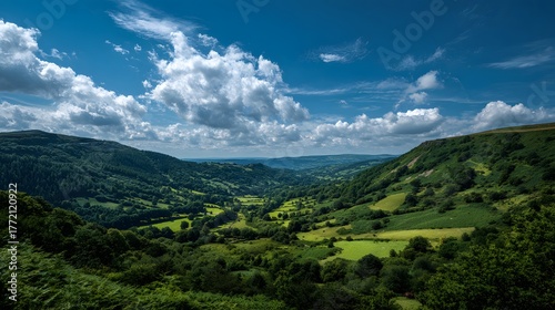 Fototapeta Naklejka Na Ścianę i Meble -  Rolling green hillsides define a wide valley beneath a dramatic blue sky with scattered clouds.