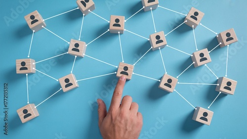 Hand pointing at connected wooden people icons on blue background, social network, team management concept.