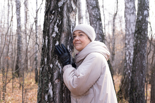 Middle-aged woman hugs tree in park. Spiritual healing, love of nature. Energy recharge in the forest. Happy adult woman hugs tree and smiles during autumn season outdoors. Natural lifes