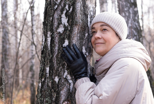Middle-aged woman hugs tree in park. Spiritual healing, love of nature. Energy recharge in the forest. Happy adult woman hugs tree and smiles during autumn season outdoors. Natural lifes