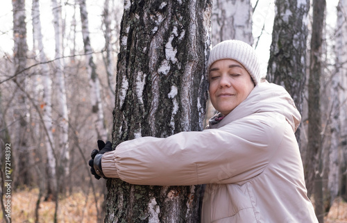 Middle-aged woman hugs tree in park. Spiritual healing, love of nature. Energy recharge in the forest. Happy adult woman hugs tree and smiles during autumn season outdoors. Natural lifes