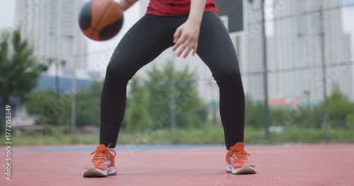 Female basketball player practicing dribbling on outdoor court, showcasing athletic legs and focus in dynamic action shot