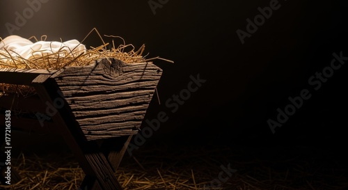 Close-up of a rustic wooden manger with hay and cloth in a dark, dramatically lit setting
