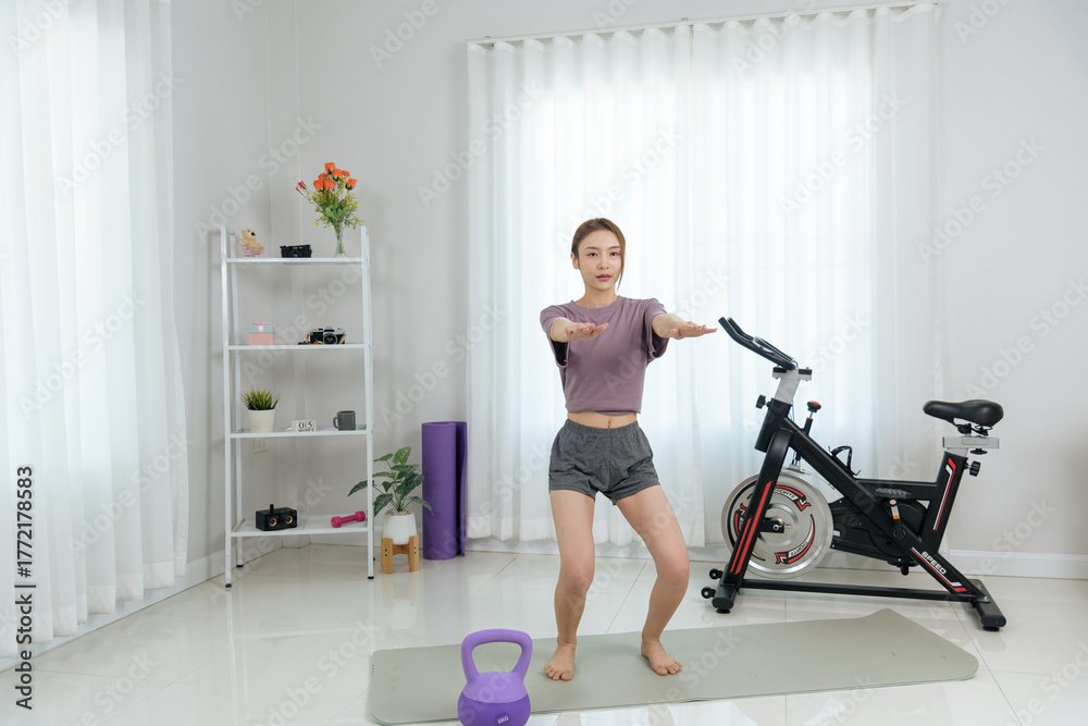 Fototapeta premium Young happy woman enjoys home activity, people engaging in fitness training, indoor workout includes yoga mat kettlebell and spin bike equipment