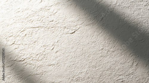 A minimalist background of a rough, off-white textured wall with soft diagonal shadows cast by natural light.