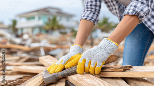 Worker wearing gloves is cleaning up wooden debris in hurricane aftermath showing storm cleanup efforts with determination and care in damaged residential area