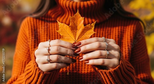 Woman in orange sweater holding autumn leaf