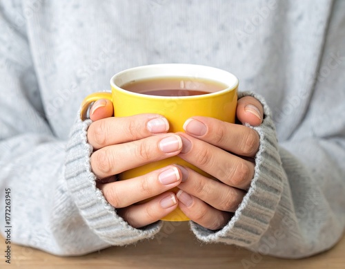 Hands holding a yellow mug of tea, wrapped in a gray sweater