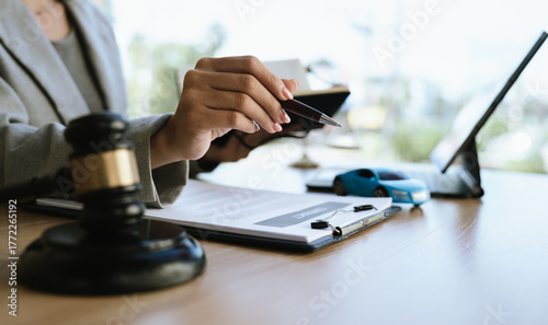 A lawyer signing a car contract with a gavel and a toy car on the desk, symbolizing car law, insurance, or legal agreement.