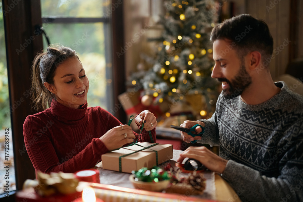 Fototapeta premium Young smiling couple wrapping Christmas presents at home.