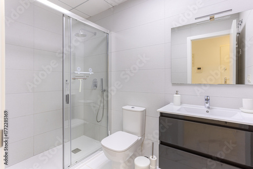 Modern bathroom with walk-in glass shower, toilet, and glossy vanity with mirror