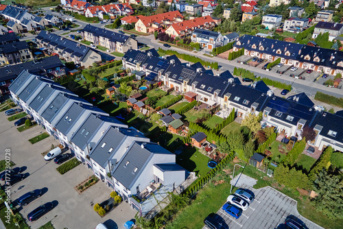 Aerial view of modern housing estate with houses, gardens and parked cars in urban neighborhood on sunny day. Modern residential area with rows of townhouses