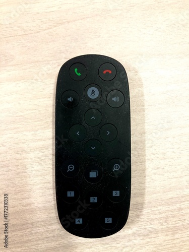 modern black conference remote control placed on a light wooden surface