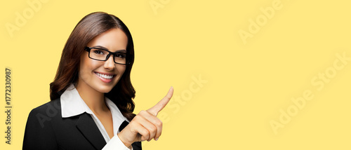 Image - happy smiling business woman wear eye glasses spectacles showing. Cute businesswoman pointing finger, advertise make positive success gesture isolated yellow background with free ad text space