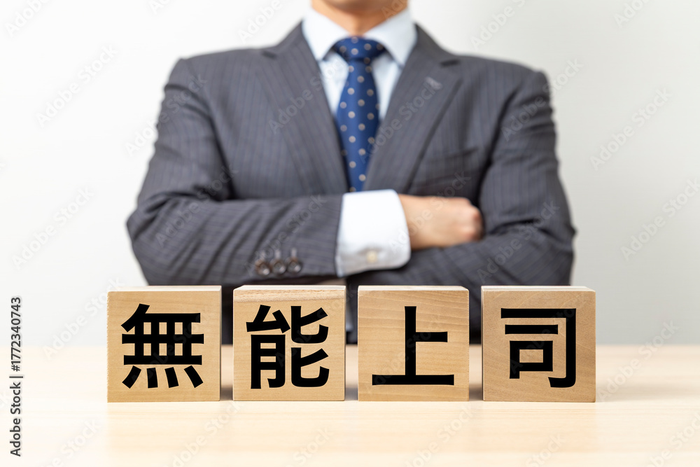 Obraz premium 「無能上司」と書かれたブロックと腕組みをするビジネスマン