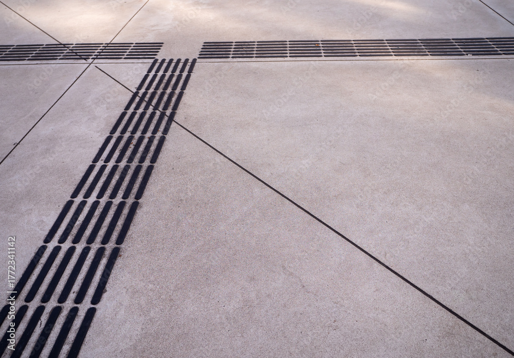 Fototapeta premium Tactile guiding strips on a concrete pavement forming a crossing pattern, designed to assist visually impaired pedestrians in an urban public space.