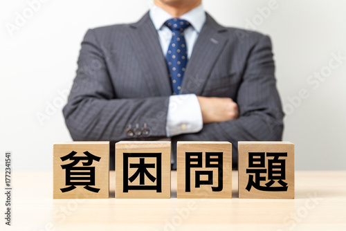 Photos 「貧困問題」と書かれたブロックと腕組みをするビジネスマン