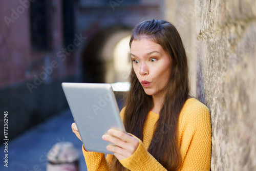A Surprised Young Woman Engaged with Her Tablet While in an Urban Setting Filled with Life