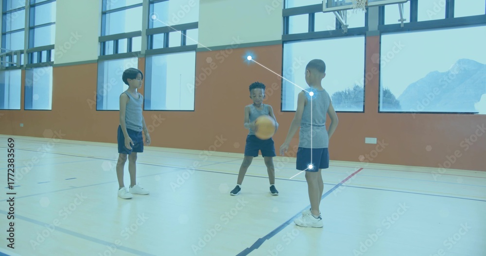 Fototapeta premium Dribbling basketball, three boys wearing grey jerseys and navy shorts on gym court near hoop
