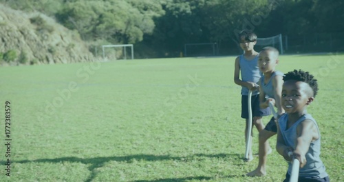 Three friends playing tug-of-war with long rope on grass soccer field near goal posts, copy space