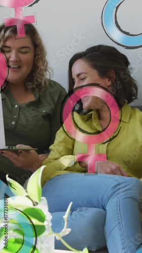 Animation of male and female symbols over lesbian couple using laptop