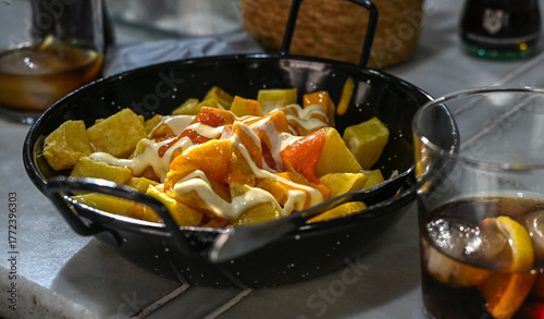Glass of cola with lemon beside a plate of patatas bravas, the classic Spanish tapas dish of fried potatoes with spicy sauce and mayonnaise,