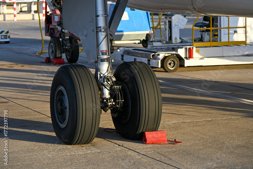 Close-up of an aircraft landing gear with chocks securing the wheels on the airport tarmac.