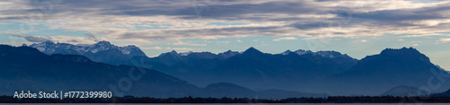 Dramatic panoramic view over the dark waters of Lake Constance (Bodensee) near Lindau, with the silhouette of the Swiss or Austrian Alps beneath a cloudy, moody sky