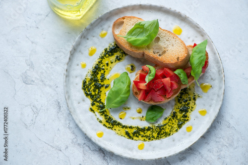 Grey plate with tomato bruschettas and basil oil, horizontal shot on a white stone background, high angle view