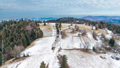 Φωτογραφία A tranquil winter panorama of Beskid Mały in southern Poland, where snowy meadows meet evergreen forests and rolling mountain hills under a serene, cloud-streaked sky