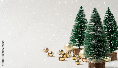 Snowy Christmas scene with miniature fir trees and scattered gold baubles on soft snow background with copy space - atmospheric holiday mockup and festive product display.