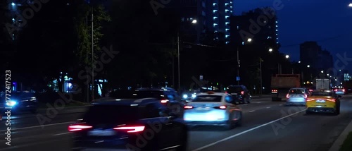 Evening city traffic on a busy multi-lane street with blurred headlights and taillights, modern urban buildings in the background, night transportation concept, fast-moving cars and highway motion 