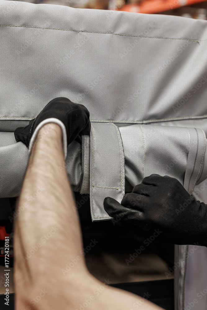 Fototapeta premium Close-up of gloved hands fastening a heavy-duty Velcro strap on a gray industrial textile cover, set in a warehouse environment