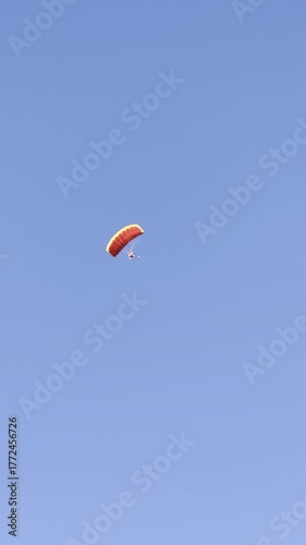 A parachutist flying in a parachute against a blue sky. A parachute jump, seen from the ground. Gliding under a parachute canopy