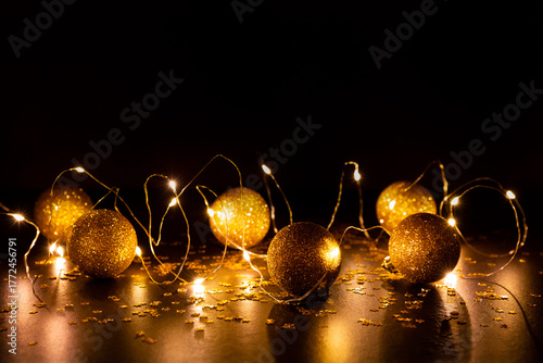 Guirlande lumineuse scintillante avec boules de Noël dorées à paillettes, posées sur un  fond brun foncé avec des étoiles dorées brillantes 